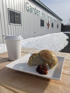 Coffee in a to go cup with cut open bun filled with scrambled eggs on a picnic table outside of of Garden Hill Farmers Market 