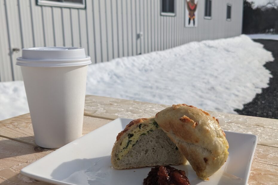 Coffee in a to go cup with cut open bun filled with scrambled eggs on a picnic table outside of of Garden Hill Farmers Market